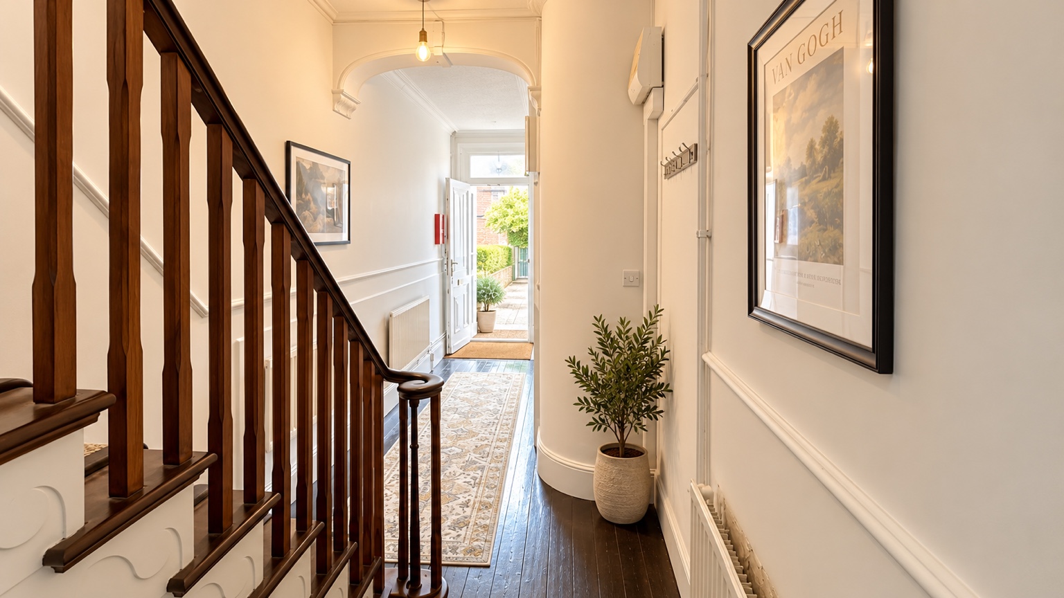 Hallway with a wooden staircase, framed artwork and a patterned runner
